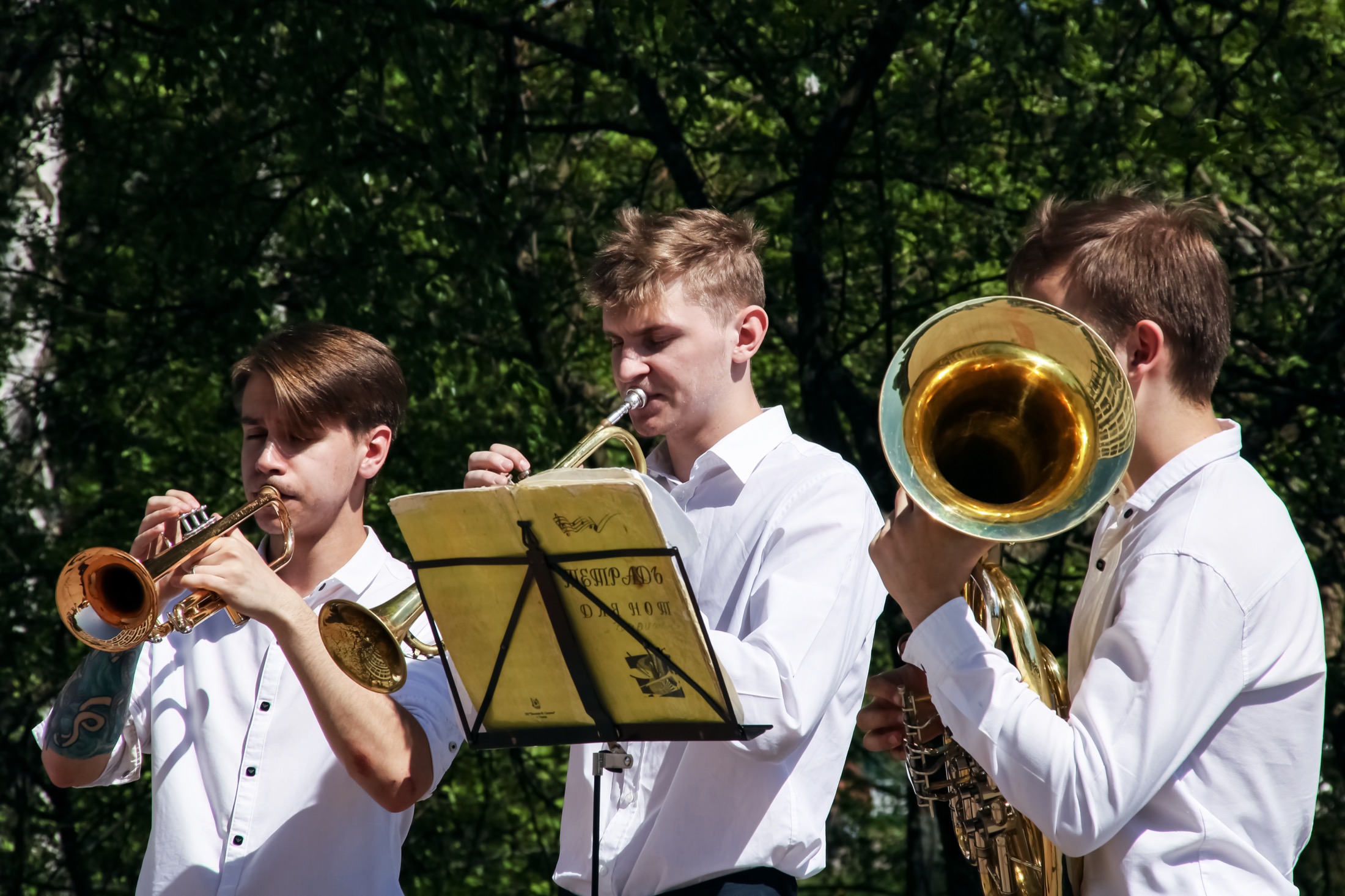 Drei junge Blechbläser musizieren gemeinsam im Freien